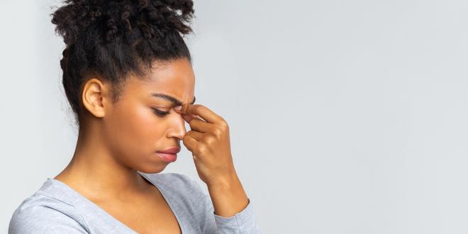 a young woman holding the bridge of her nose due to sinus pain