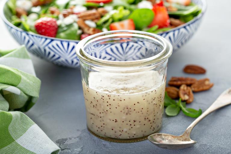 a jar of poppy seed dressing in front of a strawberry salad